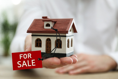 Real estate agent holding house model with SALE label indoors, closeup