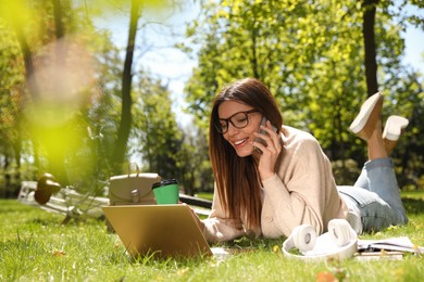 Photo of Woman talking on phone while working with laptop in park