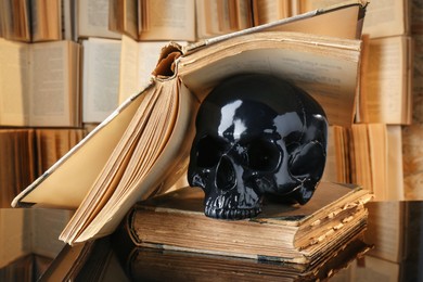Photo of Black human skull and old books on mirror table