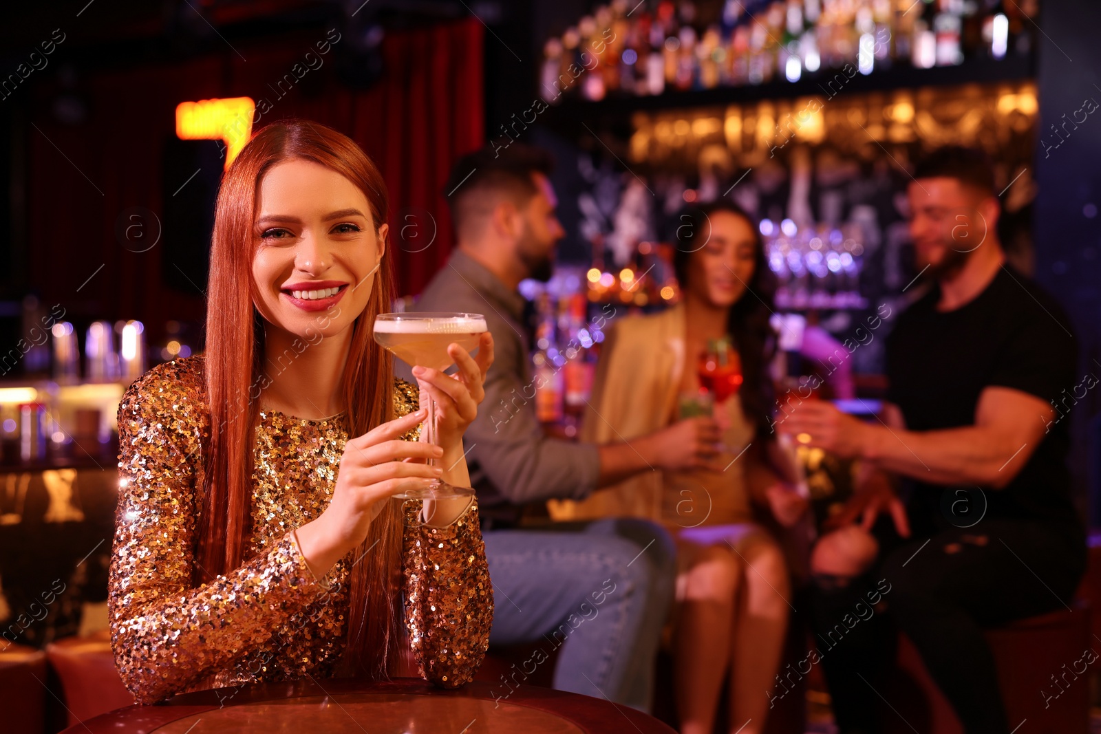 Photo of Friends spending time together in bar. Beautiful woman with fresh alcoholic cocktail at table, space for text