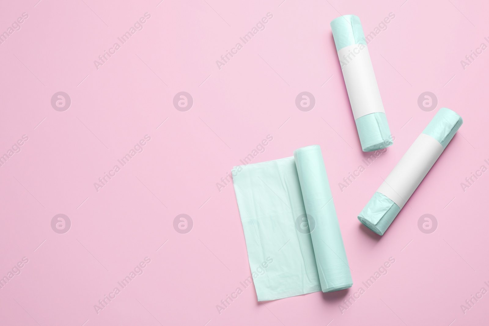 Photo of Rolls of garbage bags on pink background, flat lay. Space for text