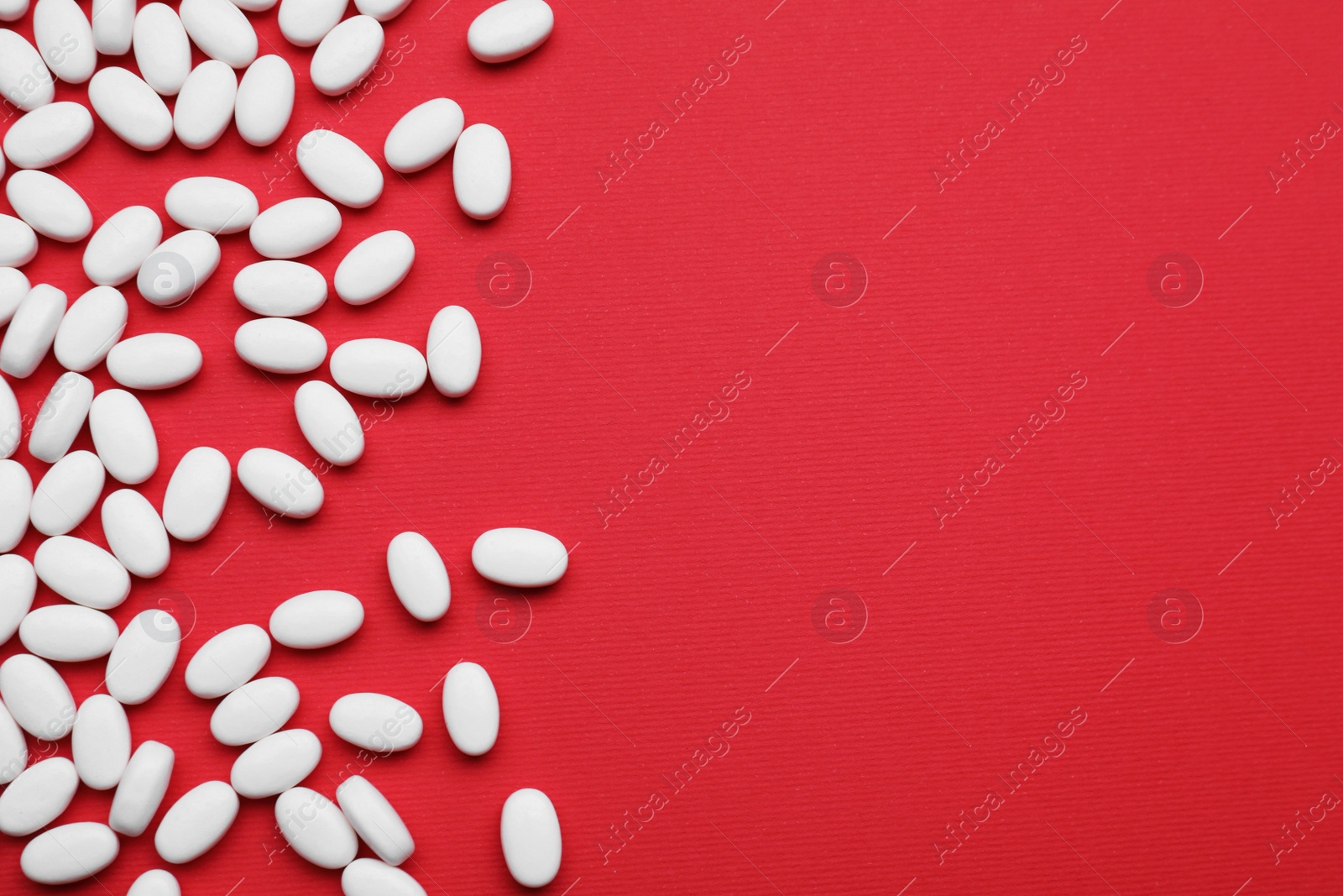 Photo of Many white dragee candies on red background, flat lay. Space for text