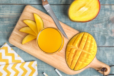 Glass of fresh mango juice and cut fruits on wooden table, top view