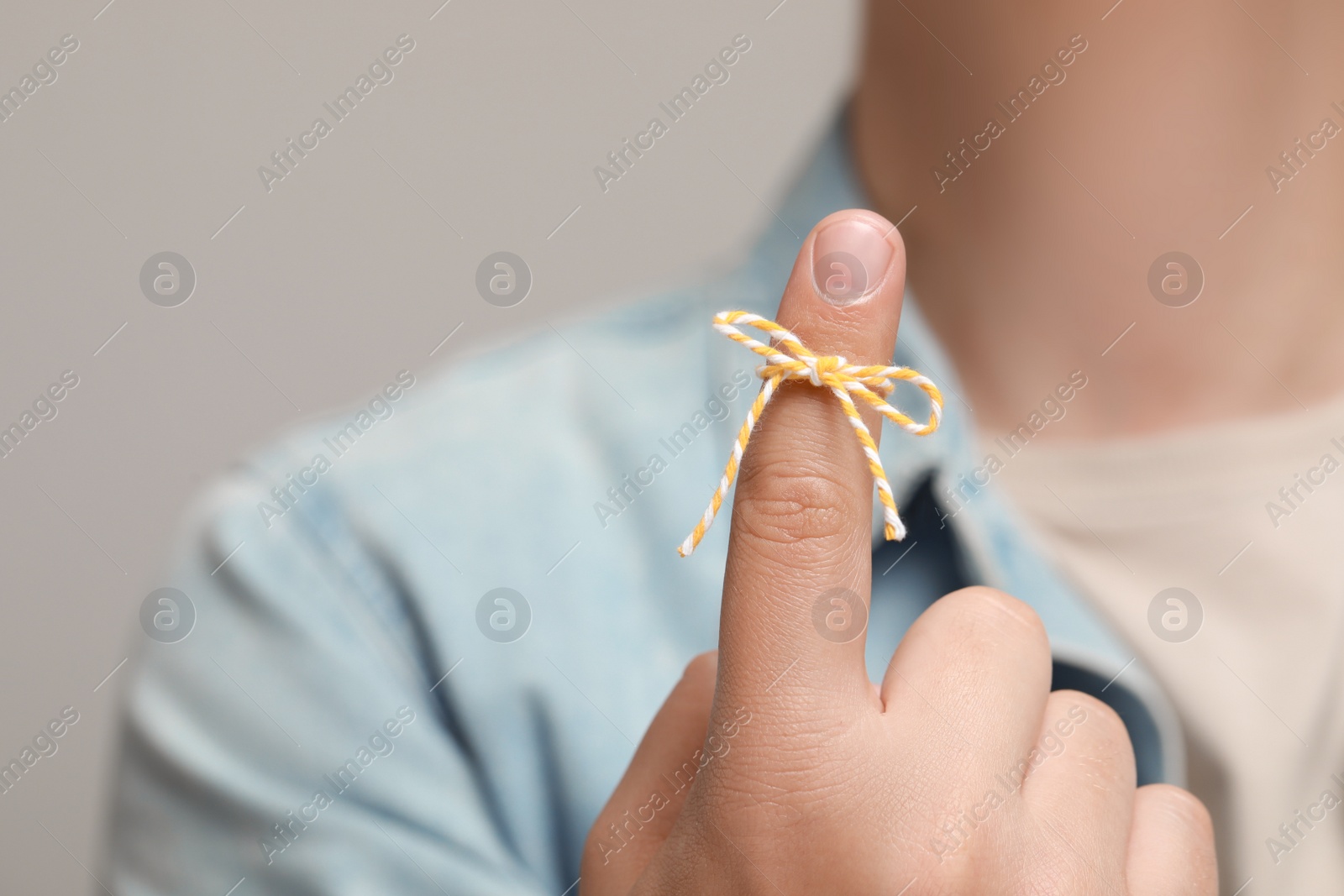 Photo of Man showing index finger with tied bow as reminder against light grey background, focus on hand