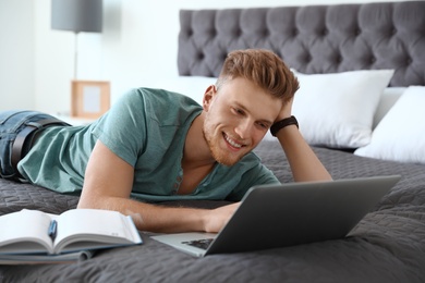 Photo of Young man using laptop while lying on bed at home