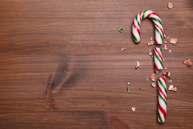 Photo of Broken sweet Christmas candy cane on wooden table, top view. Space for text