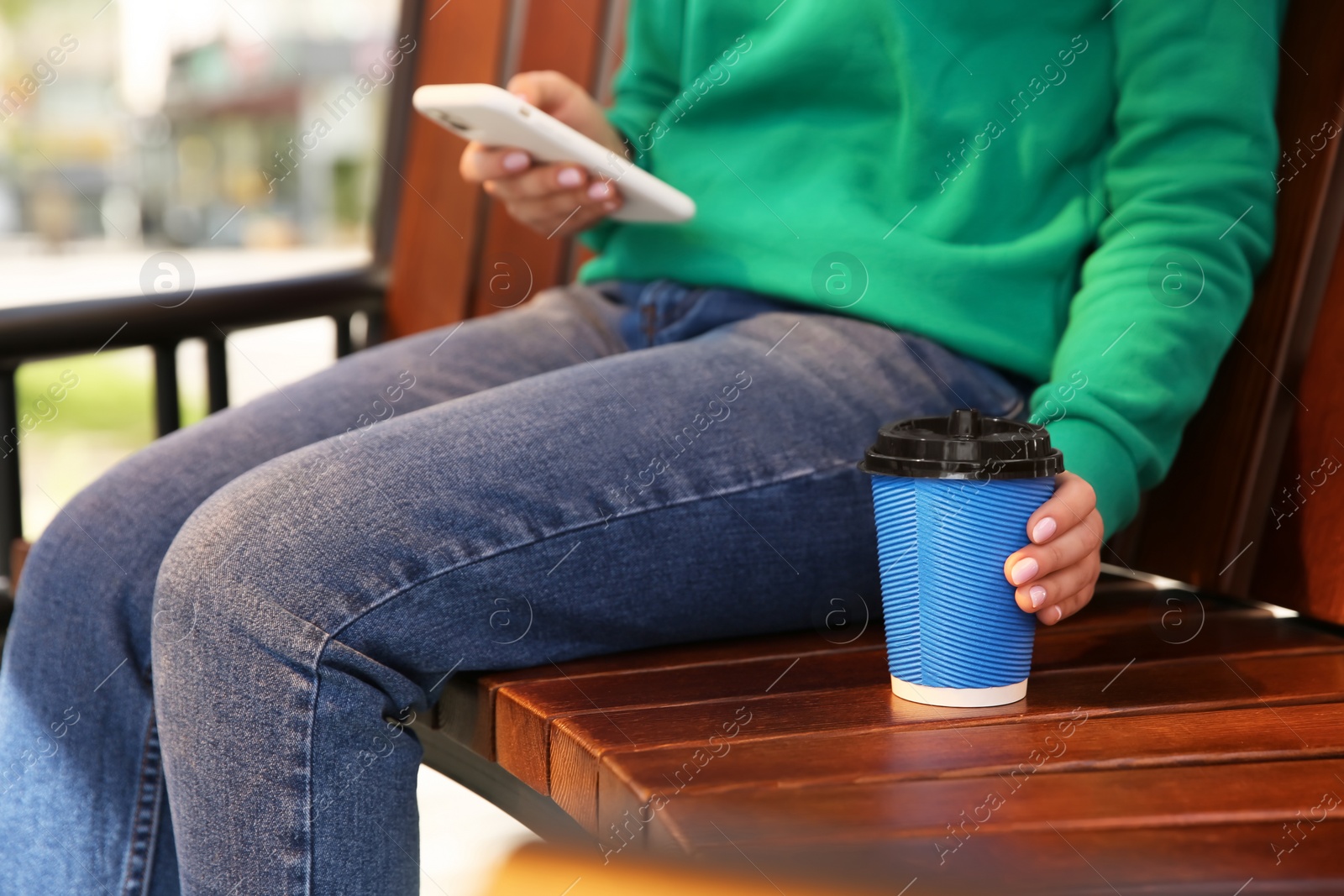 Photo of Woman with takeaway coffee cup on bench, closeup