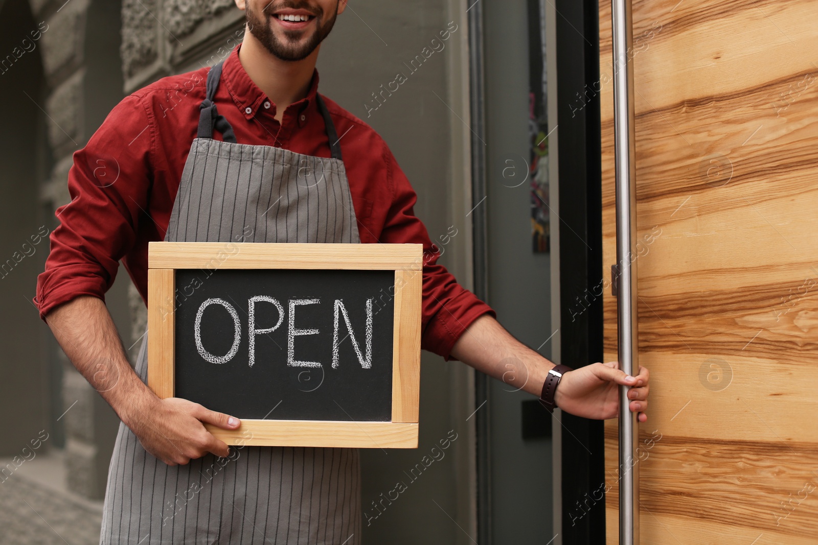 Photo of Young male business owner holding OPEN sign near his cafe, closeup