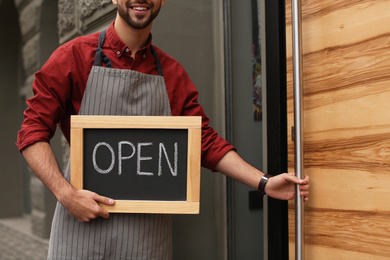 Photo of Young male business owner holding OPEN sign near his cafe, closeup