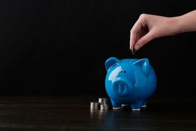 Photo of Financial savings. Woman putting coin into piggy bank at wooden table, closeup. Space for text