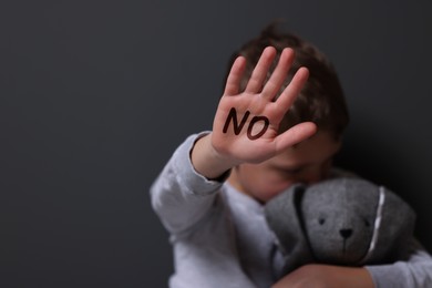 Child abuse. Boy with toy bunny making stop gesture near grey wall, selective focus. No written on his hand
