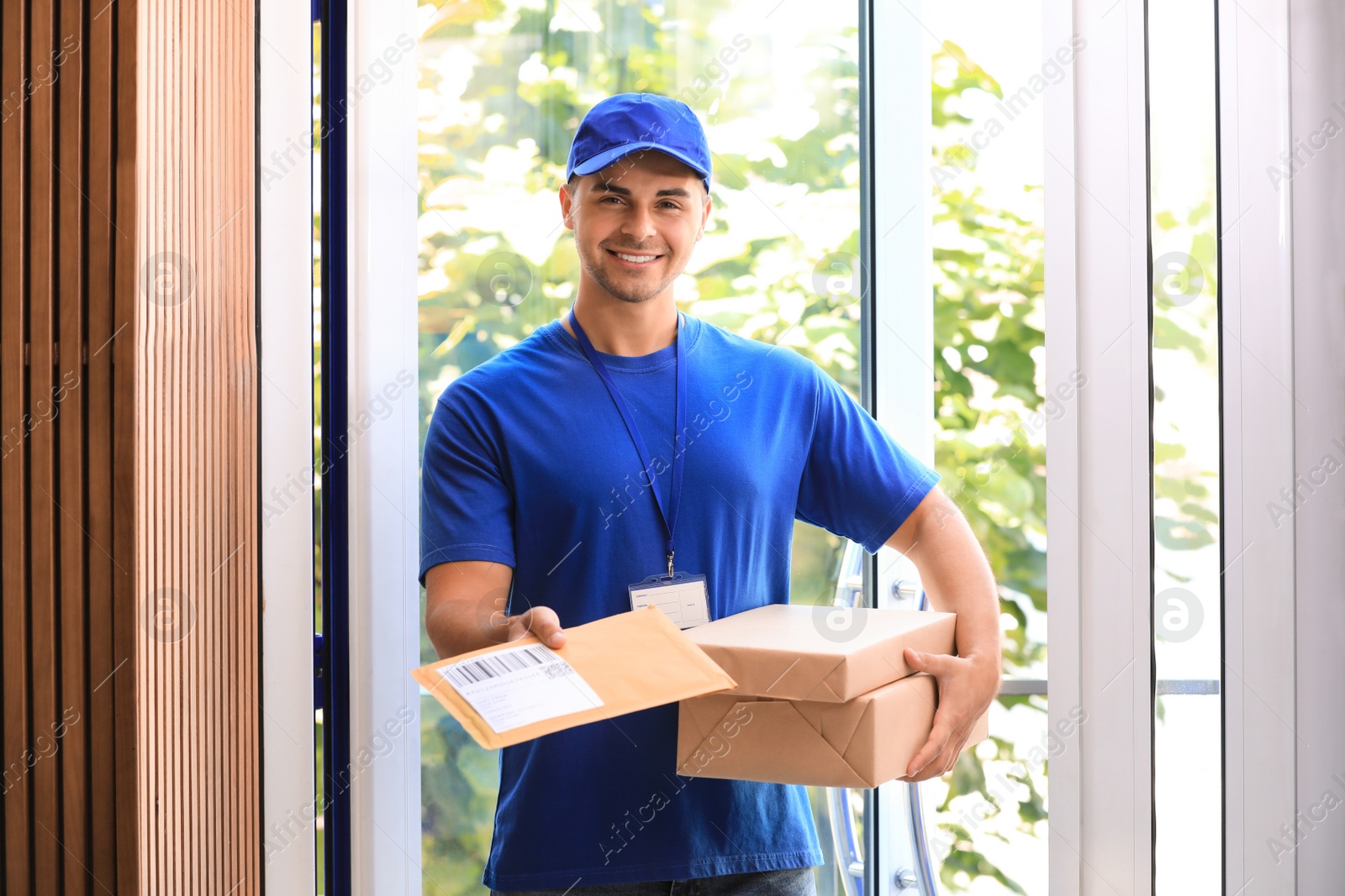 Photo of Young courier holding parcels on doorstep. Delivery service
