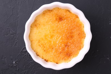 Photo of Delicious creme brulee in bowl on dark gray textured table, top view