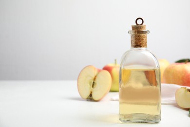 Photo of Natural apple vinegar and fresh fruits on white table. Space for text