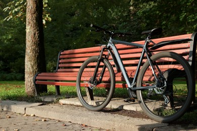 Photo of Modern bicycle near wooden bench outdoors, space for text