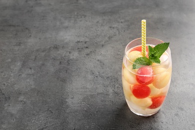 Photo of Glass of melon and watermelon ball cocktail with mint on grey table. Space for text