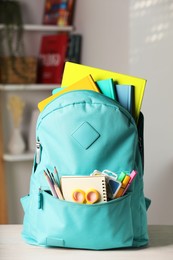 Photo of Turquoise backpack with different school stationery on white table indoors