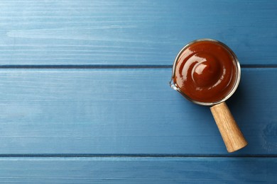 Tasty barbeque sauce on blue wooden table, top view. Space for text