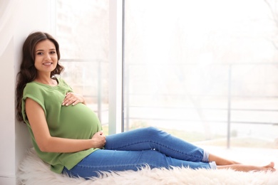 Beautiful pregnant woman sitting near window at home