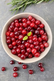 Photo of Fresh ripe cranberries in bowl and rosemary on grey table, flat lay