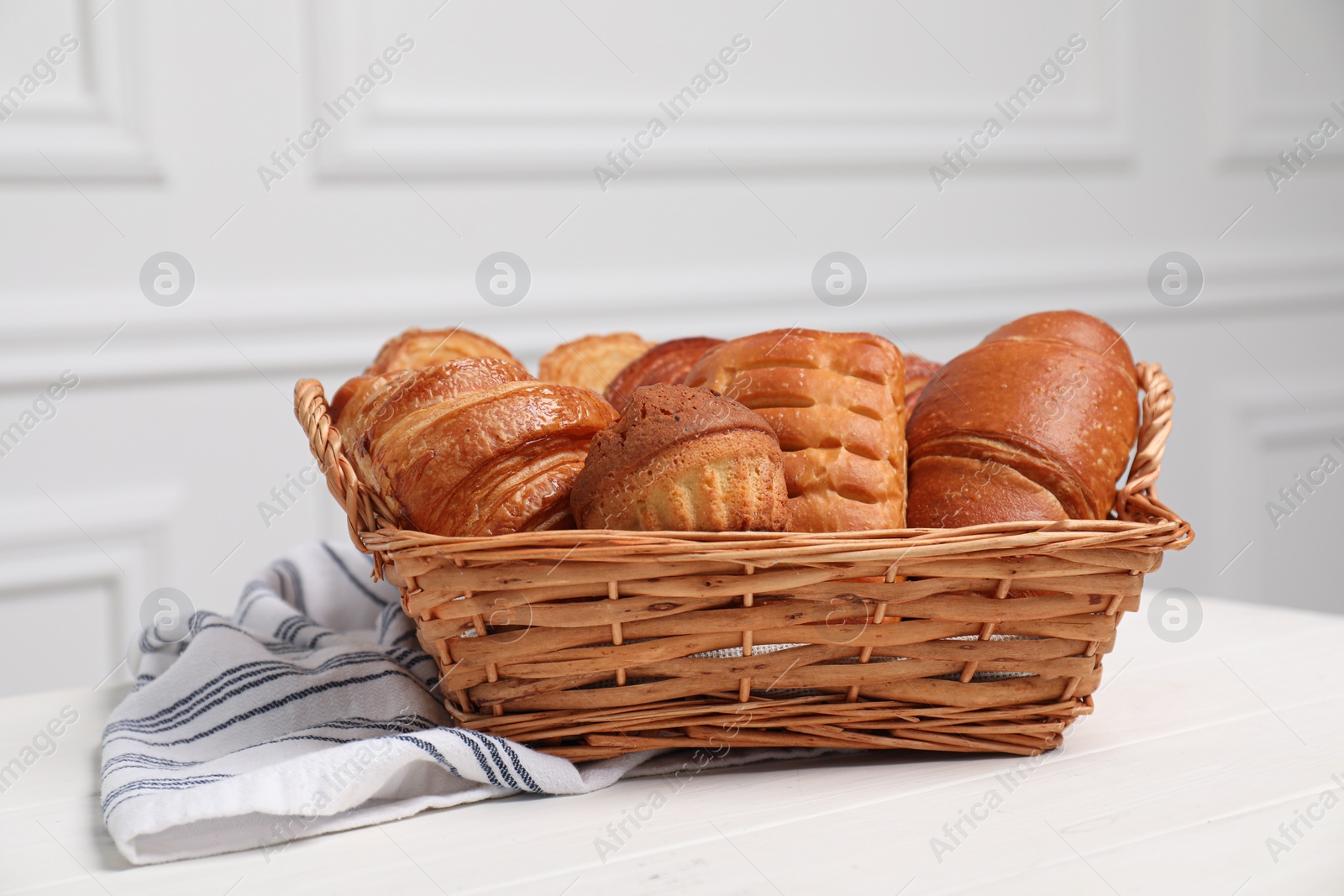 Photo of Wicker basket with different tasty freshly baked pastries on white wooden table, closeup