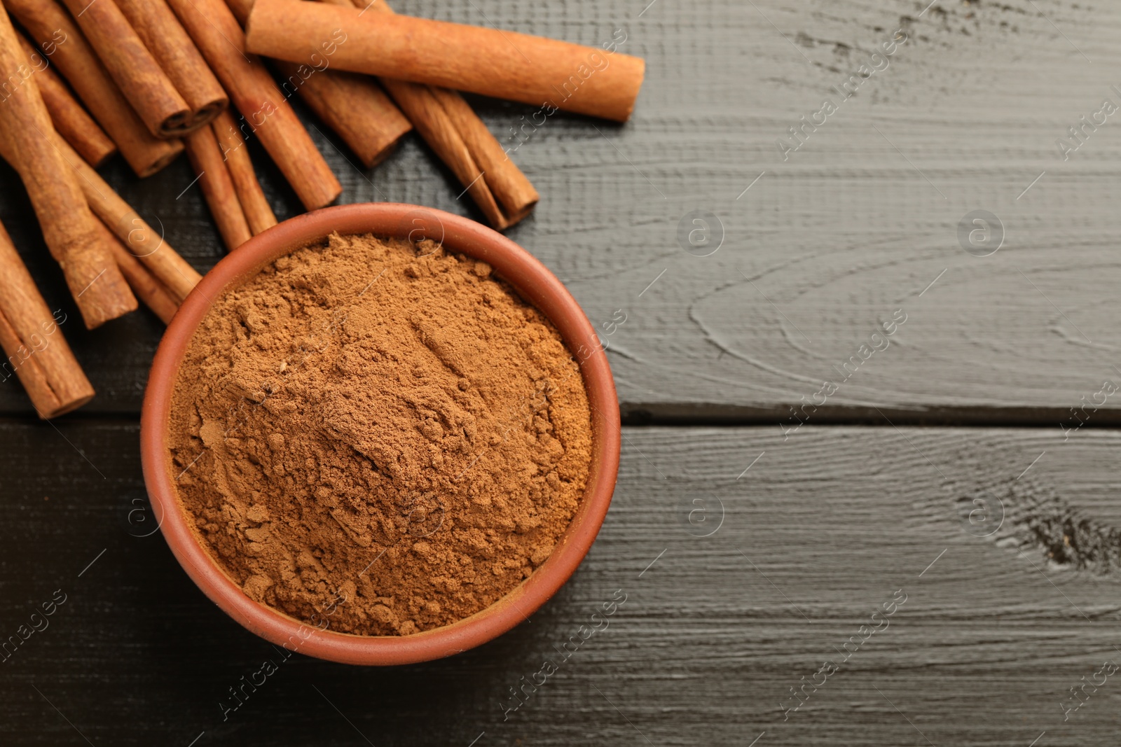 Photo of Bowl of cinnamon powder and sticks on wooden table, flat lay. Space for text