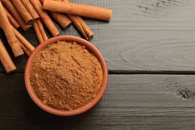 Bowl of cinnamon powder and sticks on wooden table, flat lay. Space for text