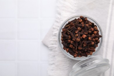 Photo of Aromatic cloves in glass jar on white tiled table, top view. Space for text