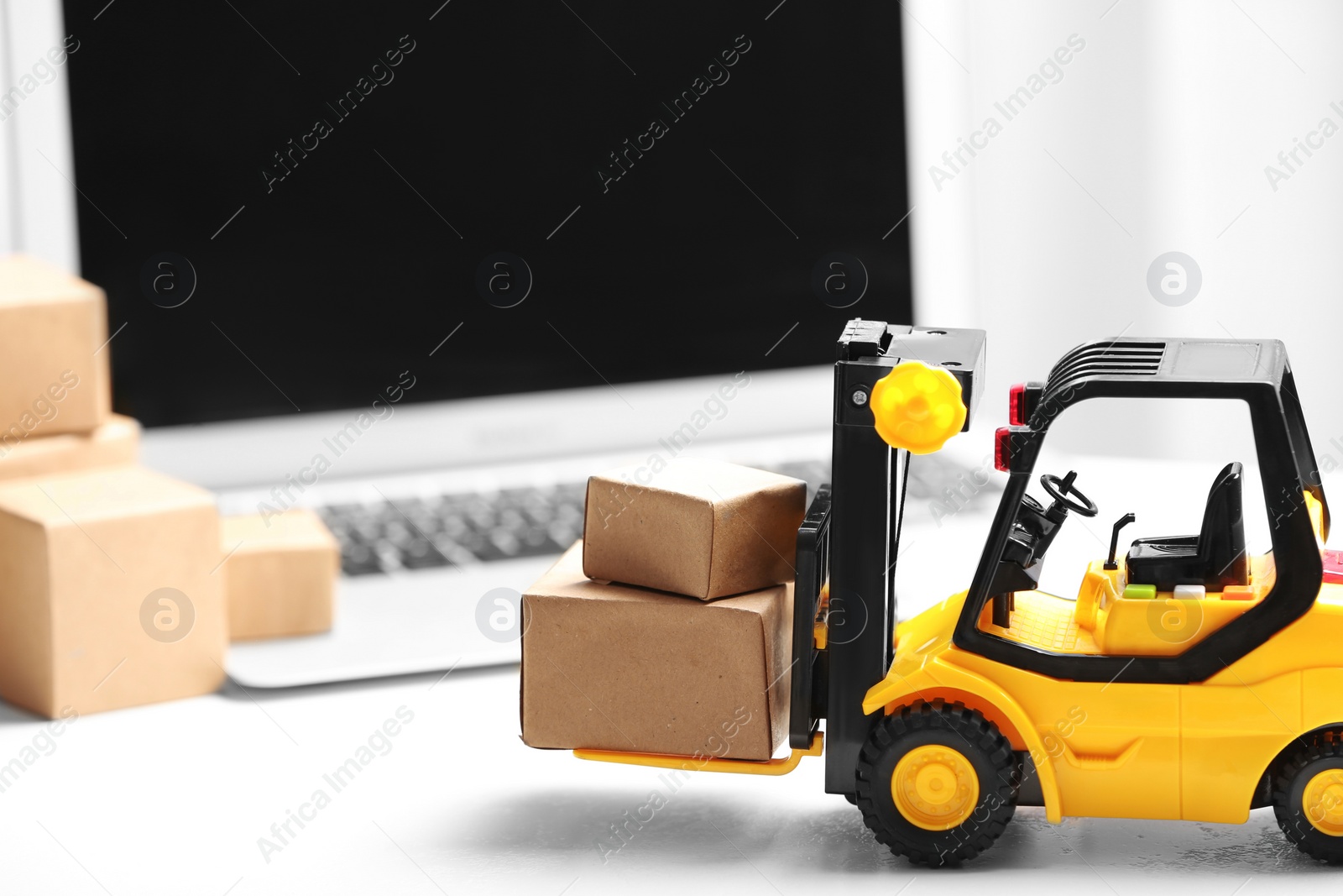 Photo of Toy forklift with boxes near laptop on table. Logistics and wholesale concept