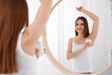 Photo of Beautiful young woman applying deodorant in bathroom