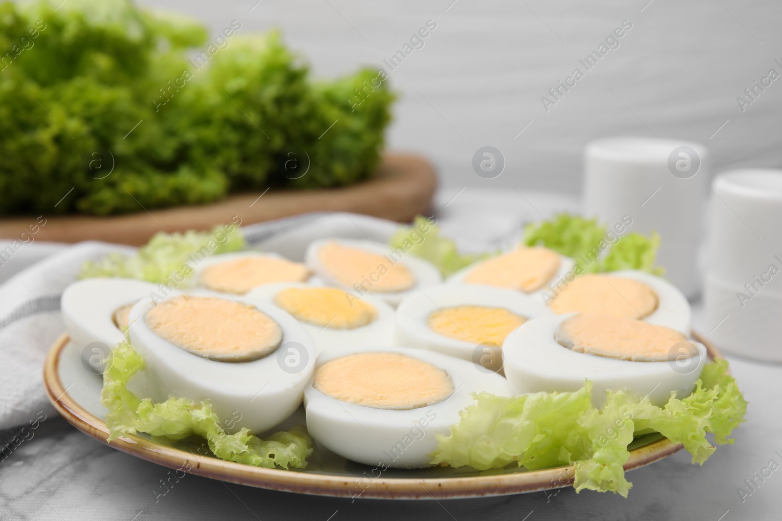 Photo of Fresh hard boiled eggs and lettuce on white marble table