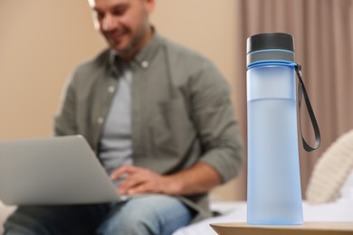 Photo of Man working with laptop indoors, focus on transparent plastic bottle of water