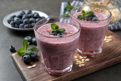 Photo of Glasses of tasty blueberry smoothie with oatmeal on dark grey table