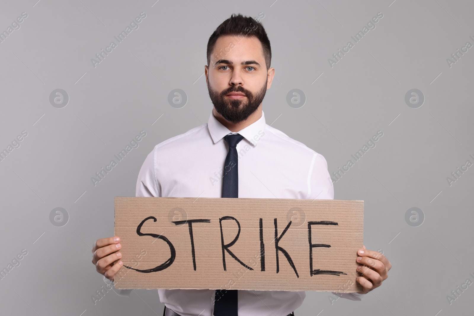 Photo of Young man holding cardboard banner with word Strike on light grey background