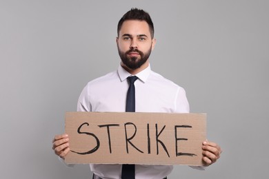 Young man holding cardboard banner with word Strike on light grey background