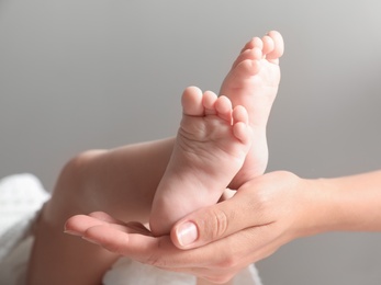 Mother holding her baby on grey background, closeup on feet