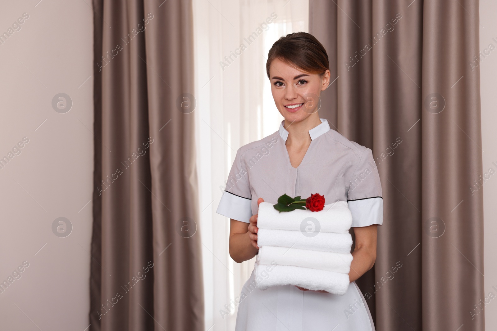 Photo of Beautiful chambermaid with stack of fresh towels in hotel room