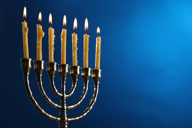 Photo of Hanukkah celebration. Menorah with burning candles on blue background, closeup and space for text