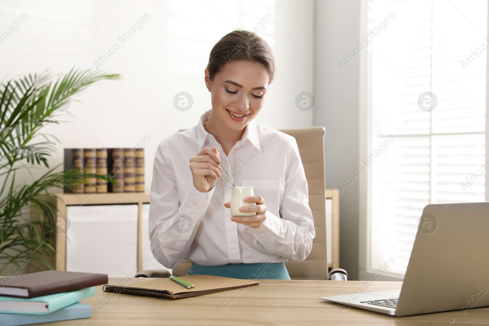 Photo of Young attractive woman with tasty yogurt at table in office