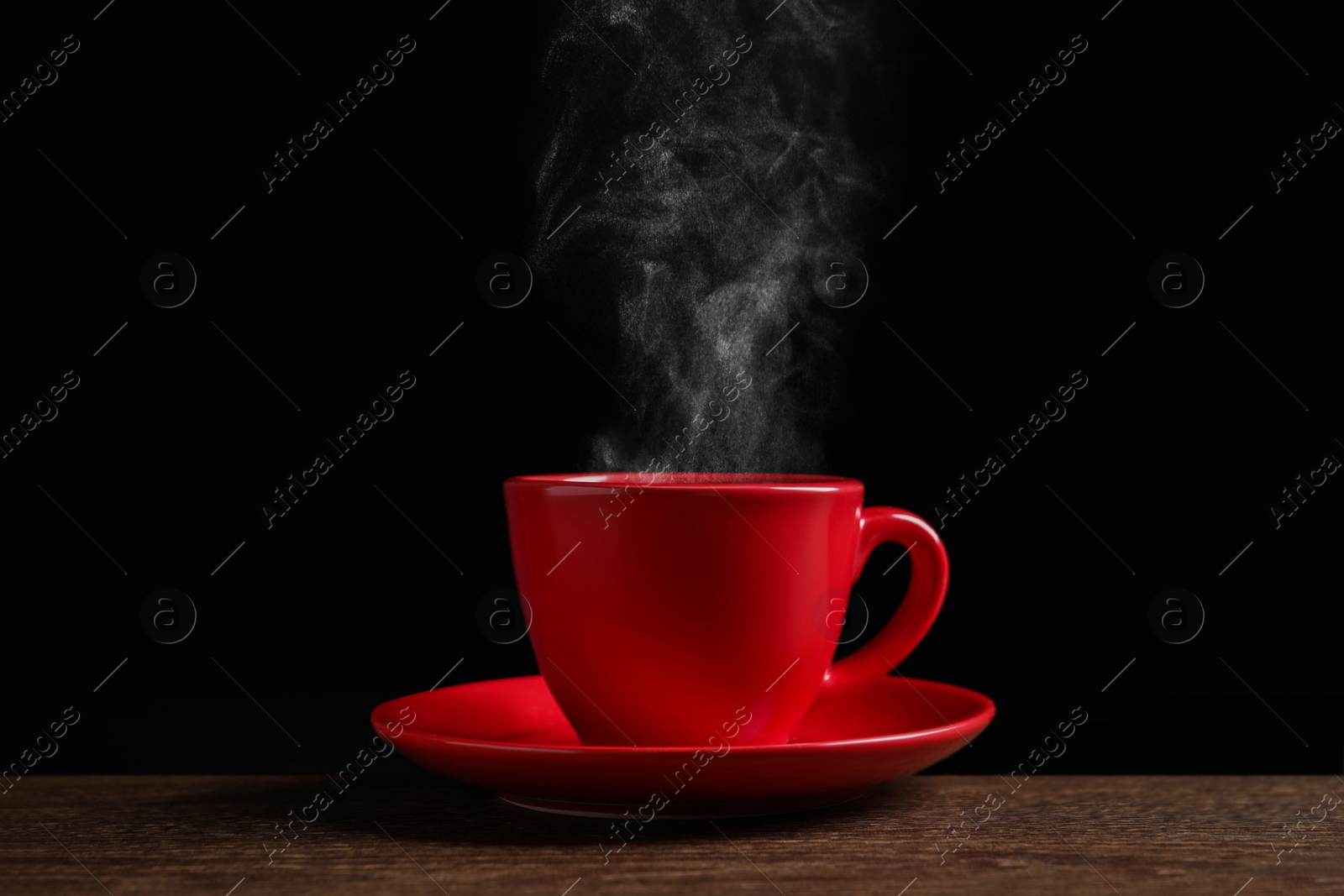 Image of Red cup with hot steaming coffee on wooden table against black background
