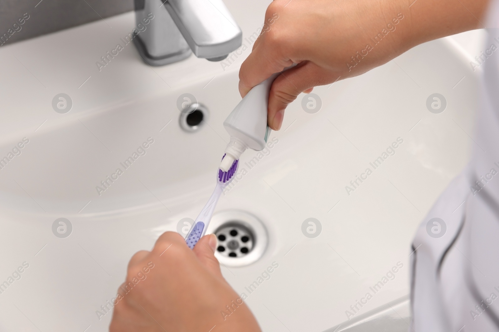 Photo of Woman applying toothpaste on brush in bathroom, closeup