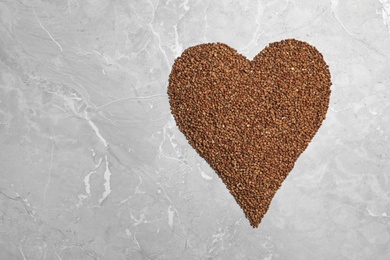 Photo of Heart made of raw buckwheat on grey background, top view. Space for text