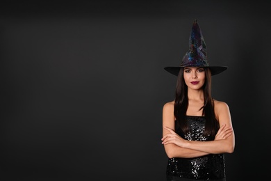 Photo of Beautiful woman wearing witch costume for Halloween party on black background, space for text