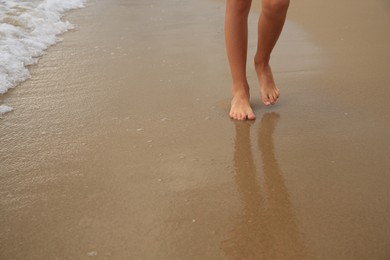 Little girl walking on sandy beach near sea, closeup. Space for text