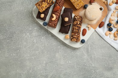 Different energy bars, nuts, blueberries and protein powder on grey table, flat lay. Space for text