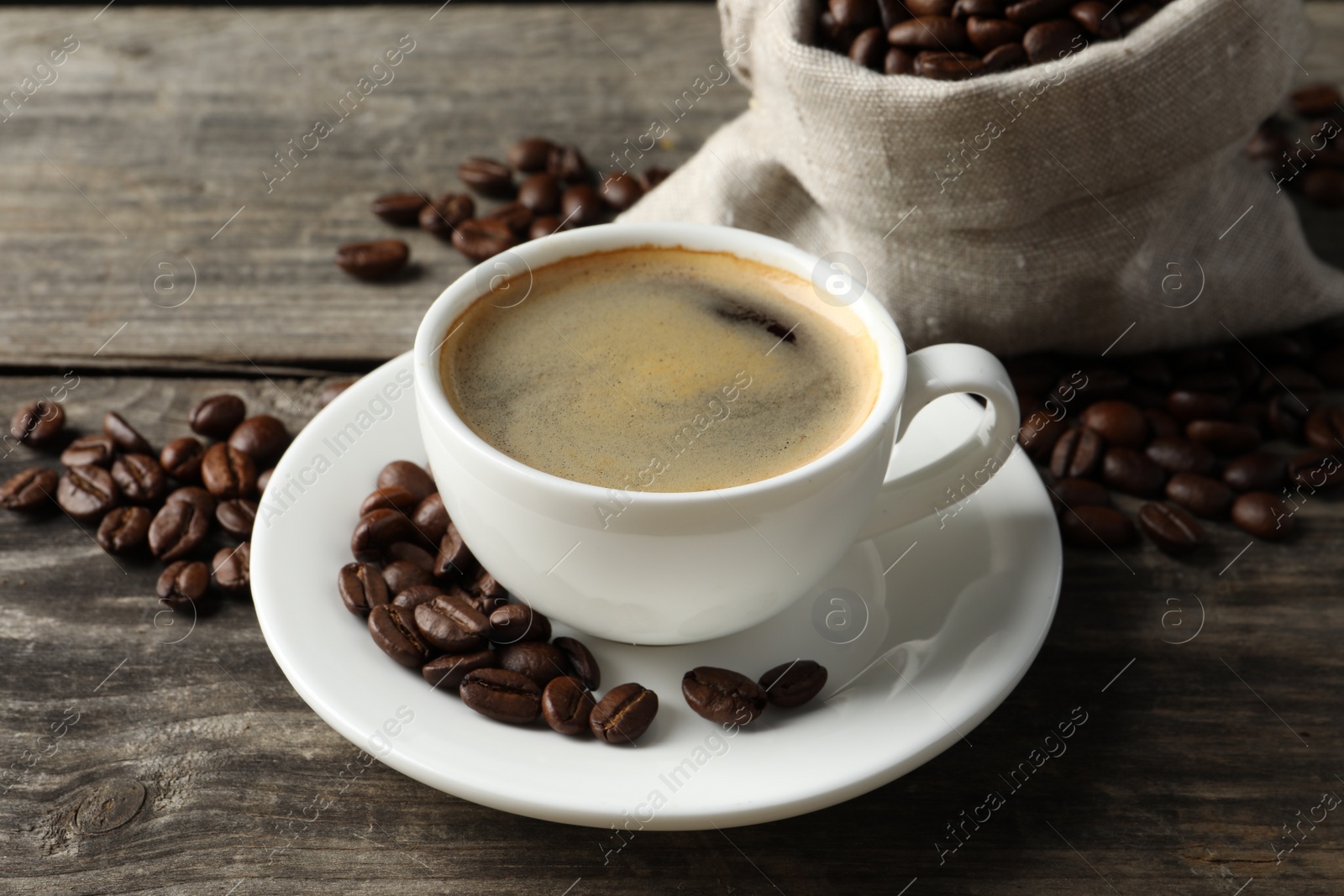 Photo of Cup of hot aromatic coffee and roasted beans on wooden table