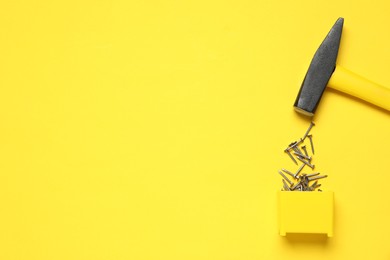 Photo of Hammer and metal nails on yellow background, top view. Space for text