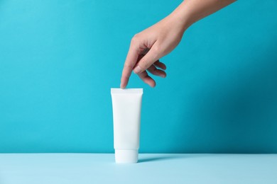 Woman with tube of hand cream at table against light blue background, closeup