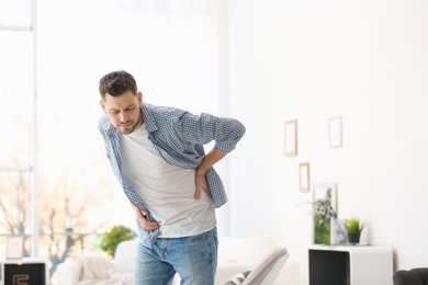 Photo of Young man suffering from back pain at home