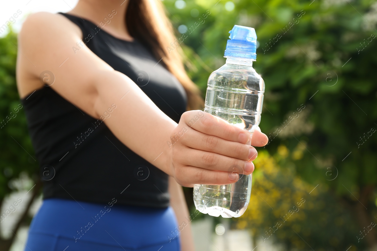 Photo of Young woman with bottle of pure water outdoors, closeup